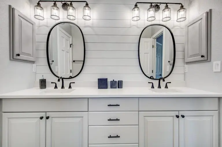 a bathroom featuring dual oval mirrors, lighting, and white cabinets.